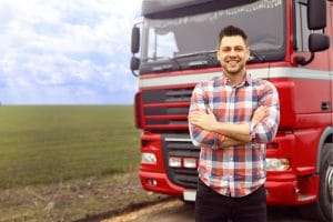 Truck driver standing in front of his red truck in the middle of a field